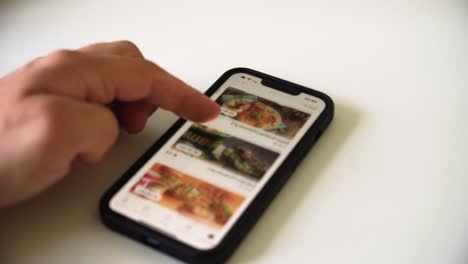 Die-Aufnahme-Der-Hand-Eines-Mannes,-Der-Durch-Die-Essensbestell-App-Auf-Einem-Smartphone-Scrollt,-Um-Das-Essen-Für-Das-Abendessen-Auszuwählen