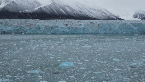 Ice-blocks-floating-on-water-in-front-of-a-glacier-with-snowcapped-mountains-in-the-background-in-the-Arctic-Sea-North-of-Svalbard