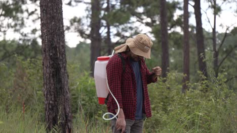 Medium-shot-of-a-man-forest-ranger-working-with-a-backpack-sprayer-in-the-forest,-he-wears-a-red-shirt-and-a-hat