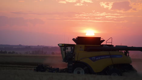 Combine-harvester-at-work-harvesting-wheat-against-vivid-sunset-sky,-aerial