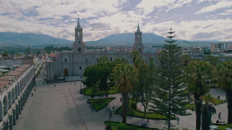 Aerial-drone-shots-above-streets-and-vegetation-leading-to-Arequipa-Cathedral,-concluding-with-a-view-of-the-snow-covered-Misti-volcano-after-a-rainy-and-cloudy-day
