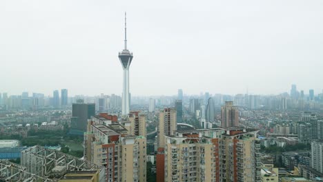 Drone-reveal-shot-of-the-West-Pearl-broadcast-tower-flying-close-to-apartment-buildings-in-Chengdu-city-on-a-hazy-day,-USA