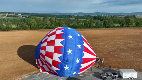 Absteigende-Drohnenaufnahme,-Die-Die-Landung-Eines-Heißluftballons-Auf-Einem-Weizenfeld-Während-Des-Sonnenuntergangs-Zeigt