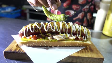 Slow-motion-shot-of-a-chef-adding-a-jalapeno-to-finish-off-the-hotdog-in-a-restaurant