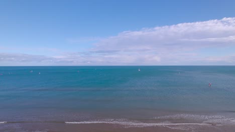 Male-walks-off-towards-waters-on-beautiful-lonely-beach,-revealing-drone-shot