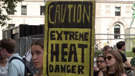 A-woman-holds-a-homemade-yellow-placard-that-reads-“Caution,-extreme-heat,-danger”-on-an-Extinction-Rebellion-protest-calling-for-an-end-to-fossil-fuel-dependency