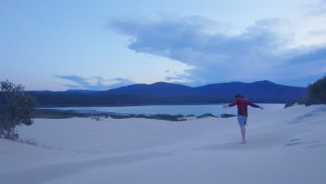 Slow-motion-shot-of-a-man-walking-out-onto-beautiful-sand-dunes-overlooking-a-lake-in-Victoria-Australia