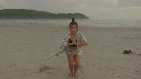 Una-Mujer-India-Practica-Yoga-Con-Gracia-En-Una-Serena-Playa-Tropical,-Combinando-Sus-Movimientos-Con-El-Ritmo-Tranquilo-Del-Mar.