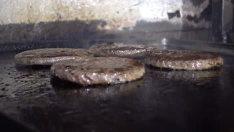 Close-up-shot-of-beef-burgers-cooking-on-an-open-top-grill-in-a-kitchen