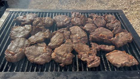 Several-medium-rare-beef-steaks-cook-on-grill-over-hot-coals-outside