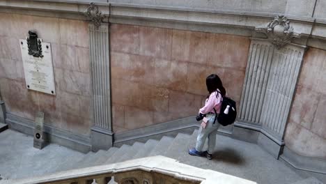 Slow-motion-wide-high-angle-shot-of-woman-walking-down-stairs-in-Palacio-da-Bolsa-in-Porto