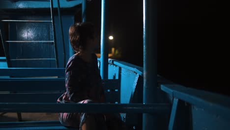 girl-sitting-on-a-boat-during-the-nighttime---Night-shot-of-a-beautiful-girl-sitting-alone-on-a-wooden-boat