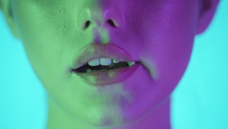 Close-up-shot-of-woman-lips-while-young-woman-chews-a-sweet-and-delicious-gum-against-turquoise-background-with-green-purple-contrast-in-her-face-in-slow-motion