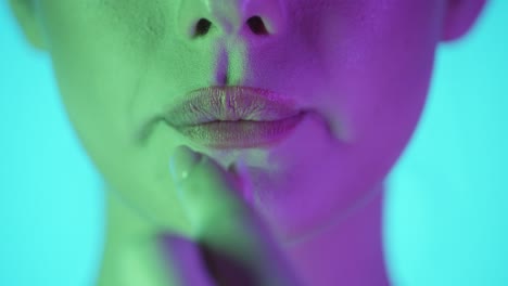 Static-slow-motion-shot-of-beautiful-young-woman-lips-while-she-puts-a-sweet-delicious-gum-in-her-mouth-and-starts-chewing-in-front-of-turquoise-background-with-green-purple-contrast-on-face