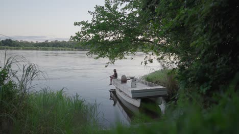 Mann-Fischt-Von-Einer-Geparkten-Boa-Am-Rande-Des-Fließenden-Sambesi-Flusses