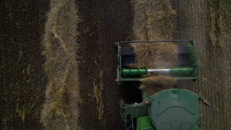 Pick-up-header-and-auger-collects-harvested-wheat-crop,-top-down-aerial