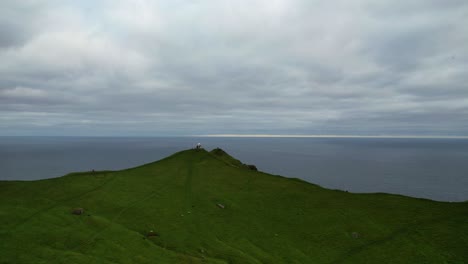 Aerial-tracking-forward-over-Kallur-Lighthouse-reveals-hiking-couple-overlooking-the-ocean,-Faroe-Islands