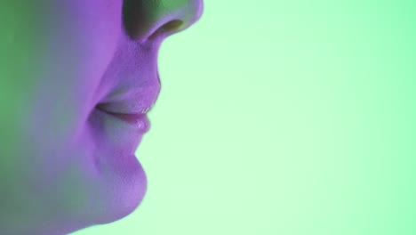 Close-up-of-beautiful-young-woman-lips-while-she-licks-her-tongue-sexy-over-her-lips-against-green-background-with-a-purple-contrast-in-her-face-in-slow-motion