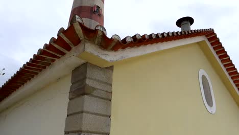 Faro-Da-Barra-Taucht-Hinter-Einem-Mit-Roten-Ziegeln-Geschmückten-Dach-In-Praia-Da-Costa-Nova,-Portugal-Auf