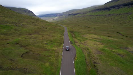 Drone-following-a-car-in-a-one-lane-Faroese-open-road-with-a-small-river-on-the-side