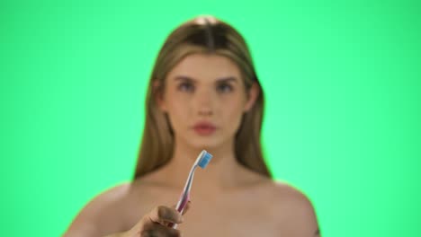 Medium-shot-of-a-pretty-young-woman-with-a-toothbrush-in-her-hand-holding-it-up-to-the-camera-and-starting-to-brush-her-teeth-for-good-dental-hygiene-and-healthy-teeth-in-front-of-green-background
