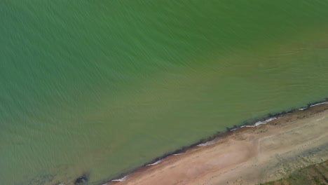 Aerial-Top-Down-View-Over-Coastal-Green-Waters-with-Beach-and-Grassy-Embankment-with-a-Drone-Tilt-Down-Shot