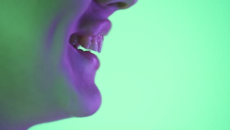 Close-up-shot-from-the-side-of-a-young-woman-smiling-and-happy-against-green-background-with-green-purple-contrast-in-her-face