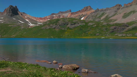 Dreamy-heavenly-Silverton-Ice-Lake-Basin-aerial-drone-cinematic-unreal-deep-sky-blue-wildflower-shoreline-Silverton-Colorado-lush-green-summer-incredible-snow-melting-Rocky-Mountains-slide-left