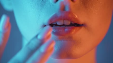 Extreme-close-up-of-a-young-woman-while-she-seductively-strokes-her-lips-with-her-finger-and-presses-them-together-with-blue-orange-contrasts-in-her-face
