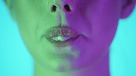 Extreme-close-up-of-a-woman-lip-chewing-a-gum-and-then-rolling-her-tongue-and-making-a-small-gum-bubble-and-smiling-in-front-of-turquoise-background-in-slow-motion