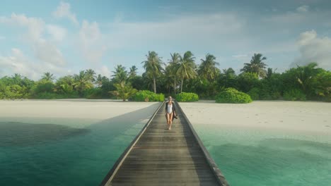 Elegant-woman-in-white-swimsuit-walking-down-wooden-pier-at-tropical-island