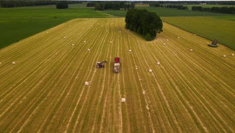 aerial-shot-of-a-tractor-working-with-a-cargo-truck-and-hay-rolls-in-a-plain-yellow-field,-tractor-putting-hay-rolls-on-the-cargo-trailer,-parallax