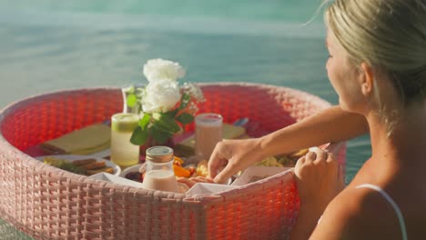 Woman-eating-tropical-food-from-floating-heart-tray-breakfast-in-pool
