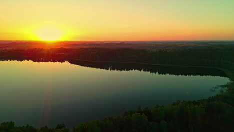 Aerial-drone-panning-shot-from-right-to-left-over-picturesque-lake-smooth-surface-at-sunset-over-forest-landscape-during-evening-time