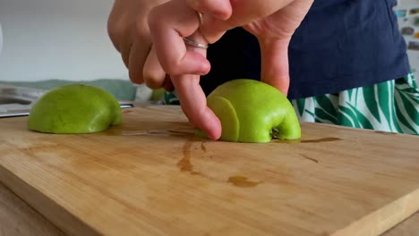 A-Woman-Demonstrates-Her-Culinary-Skills-by-Chopping-a-Fresh-Green-Apple-on-a-Wooden-Cutting-Board-in-a-Well-Lit-Kitchen,-Embracing-the-Values-of-Healthy-Eating,-Detox,-and-Diet