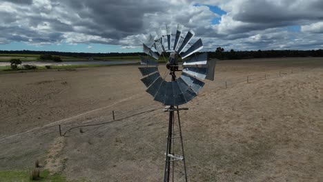 Drones-Aéreos-Orbitando-Alrededor-De-Un-Antiguo-Molino-De-Viento-Con-Palas-Giratorias-En-Una-Granja,-Región-Del-Río-Margaret-En-Australia-Occidental