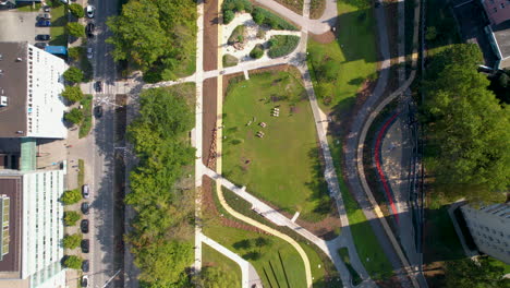 Aerial-top-down-shot-of-green-park-with-path-and-driving-cars-in-road-in-Gdynia-city-at-sunny-day