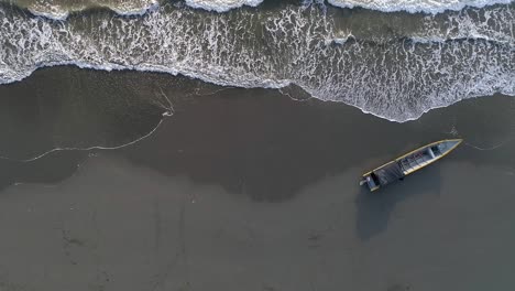 A-lone-abandoned-boat-sits-on-the-deserted-beaches-of-La-Barra,-a-beach-on-the-Colombian-Pacific-coast,-as-seen-from-above