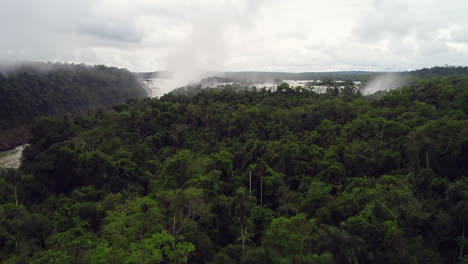 Drone-ascend-above-tropical-jungle-to-low-lying-clouds-and-mist-water-spraying-from-Iguazu-waterfall