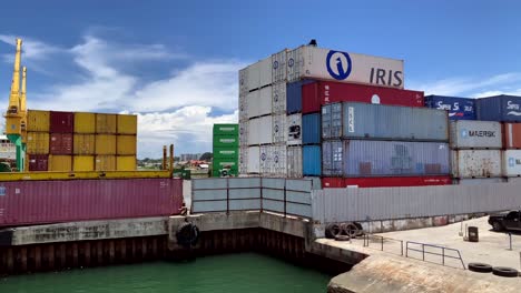 Multiple-layers-of-large-shipping-containers-are-stacked,-set-against-the-backdrop-of-massive-cargo-ships