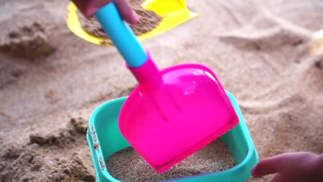 Closeup-shot-hands-of-child-playing-beach-sand-with-shovel-and-bucket