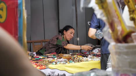 Souvenirs-Shopkeeper-woman-selling-beaded-bracelets-and-dealing-with-a-Customer,-Slowmotion,-China