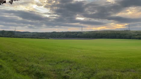 Ein-üppig-Grünes-Bauernfeld-Mit-Einem-Wolkigen-Sonnenuntergang-über-Dem-Horizont