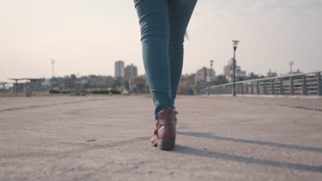 Camera-tracking-woman's-lower-body-as-she-walks-along-an-empty-street,-focused-on-her-stride,-in-brown-boots-and-jeans