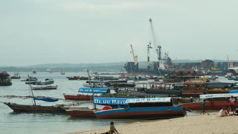 Boats-anchored-off-the-beach-in-Stone-Town,-Zanzibar,-with-the-container-port-in-the-background