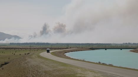 Oncoming-camper-driving-along-canal-road-with-active-wild-fire-and-gigantic-smoke-clouds-in-background
