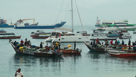 Fishing-boats-anchor-with-many-African-fishermen-off-Stone-Town-Beach,-Zanzibar,-Tanzania-on-a-cloudy-day