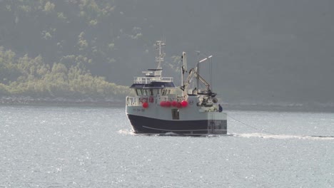 Barco-De-Pesca-Navegando-A-Lo-Largo-De-La-Isla-Husoya,-Nordland,-Noruega