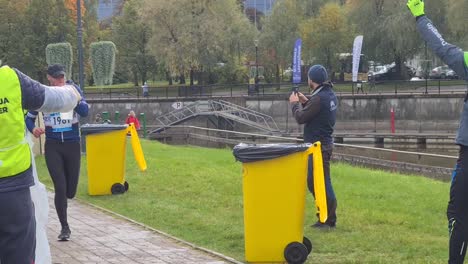 tired-runners-are-running-pass-volunteers-who-are-handing-out-cups-of-water,-used-cups-are-thrown-to-garbage-bins-for-recycling-Running-city-marathon-in-Tartu-City-center