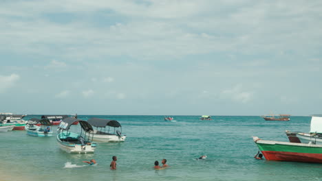 African-children-swimming-in-turquoise-water-off-the-beach-in-Stone-Town,-Zanzibar,-Tanzania